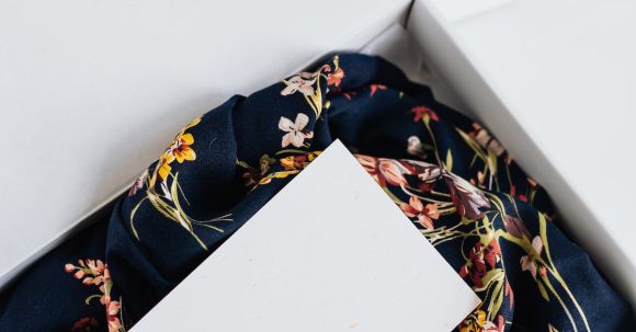 Online Outlet Stores - From above of stylish black silk floral pattern cloth with white visit card mockup placed in white carton box after receiving postal delivery of online order