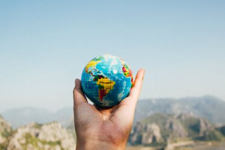 Travel Insurance - Person Holding World Globe Facing Mountain