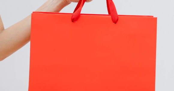 Clearance Sales - Crop unrecognizable female showing red paper shopping bag in hand against white wall
